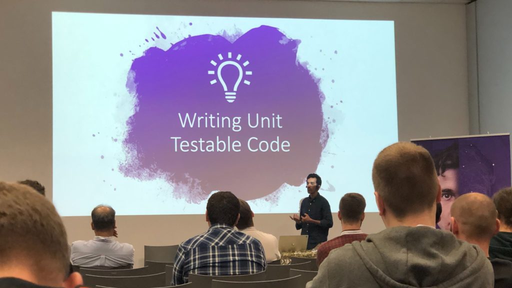 Sala konferencyjna, prelekcja o testowaniu, na ekranie prelekcji zapalona żarówka i napis Writing Unit Testable Code.