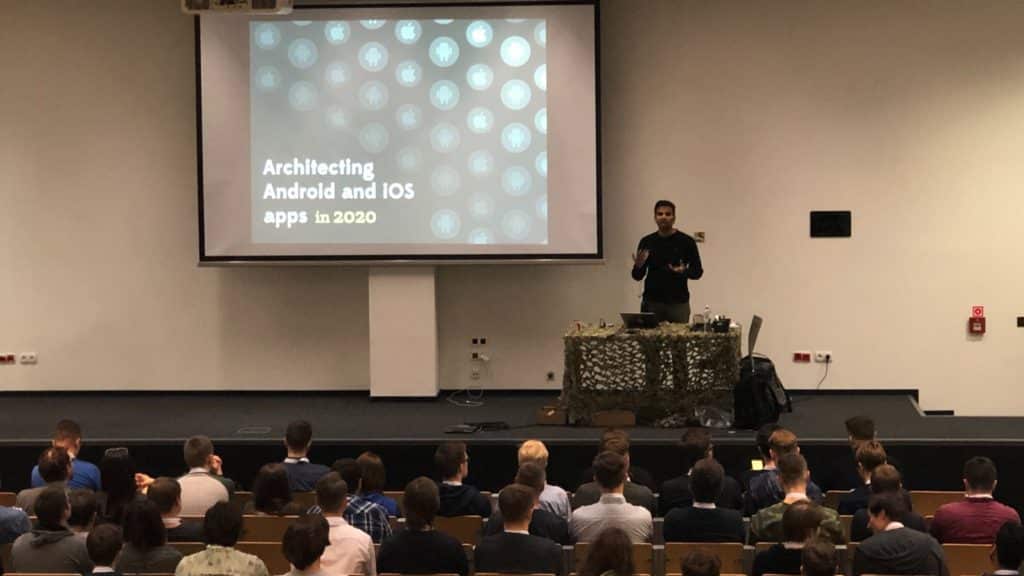 Widoczna sala pełna uczestników, prelegent, a na ekranie prelekcji wyświetlony slajd z napisem: Architecting Android and iOS apps in 2020.